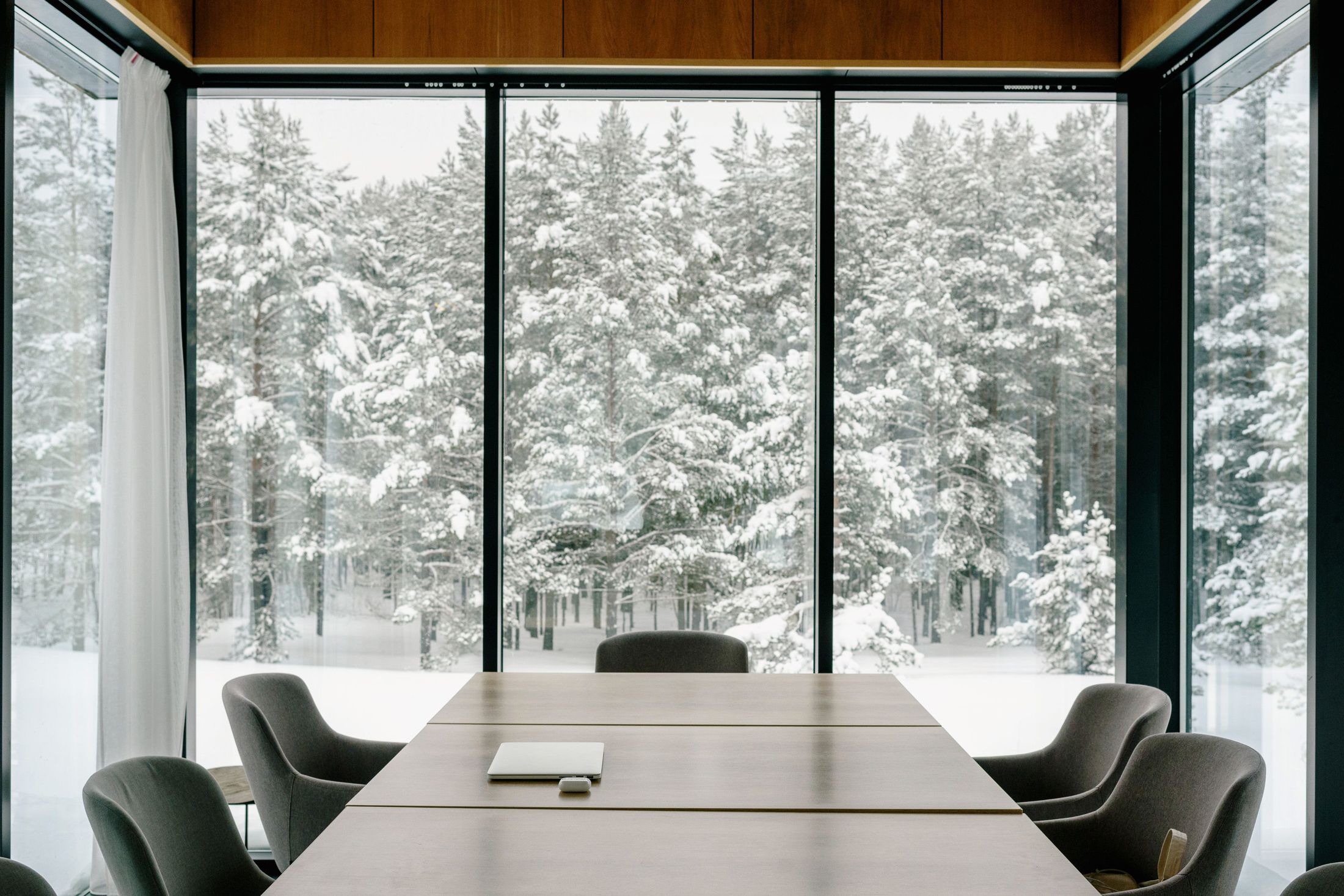 A minimal, unoccupied conference room with full-height glass overlooking a snow-covered forest.