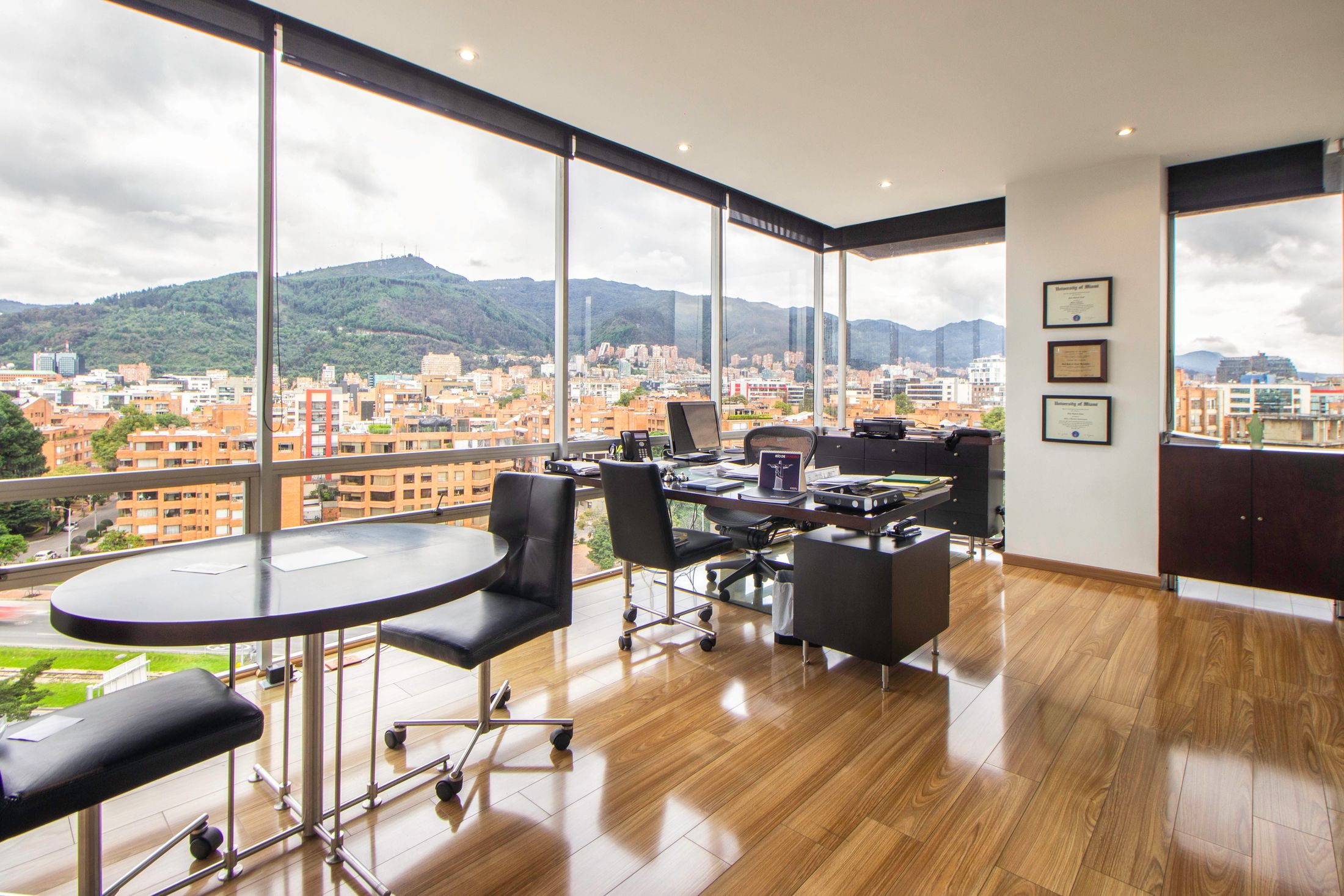 An empty corner executive office with floor-to-ceiling windows overlooking a city and distant mountains in daytime light.
